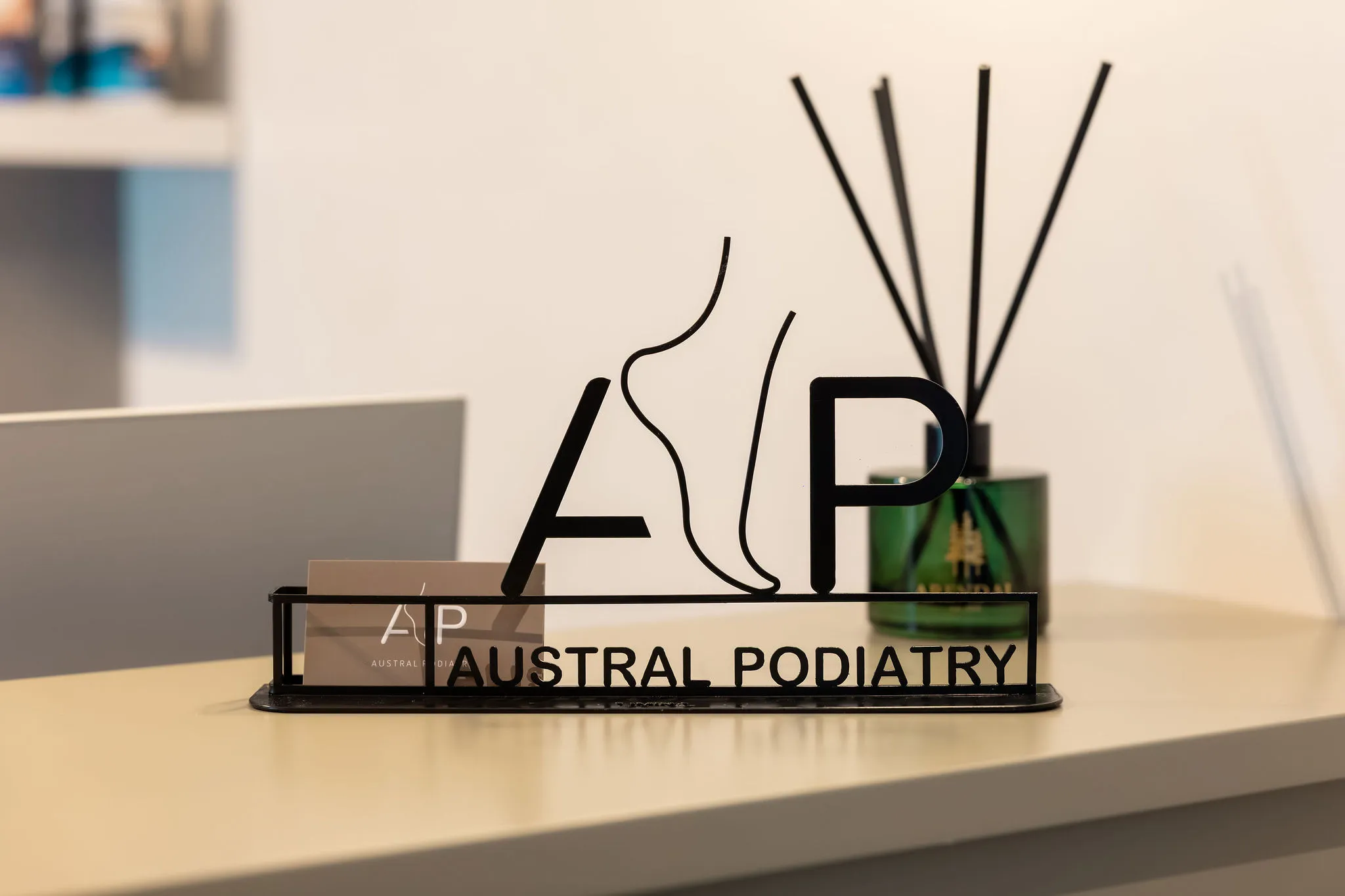 close up of black metal austral podiatry logo sign and business card holder on reception desk at podiatry clinic in austral, nsw