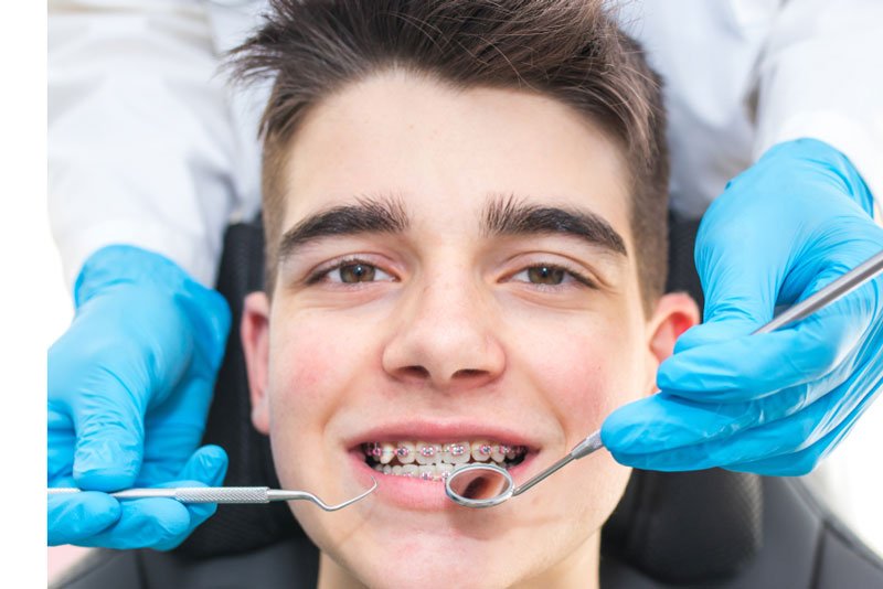 Teenage boy with braces receiving an orthodontic checkup from a dentist wearing blue gloves.
