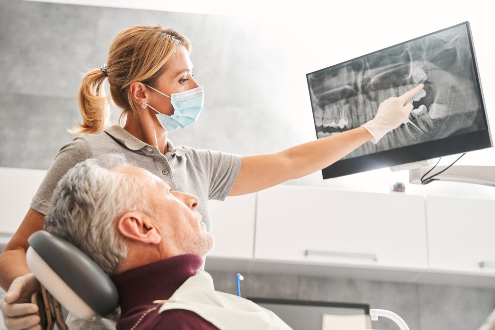 Close-up photo of a dentist placing a tooth implant into a patient's jaw, showcasing the precision and care involved in the procedure. No text on the image.