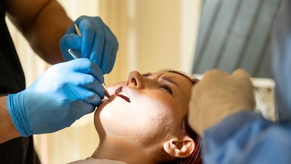 Close up image of a dentist placing a crown on a patient's tooth, with the dentist's hands and dental instruments in focus. No text on image.