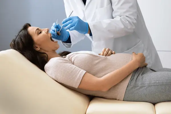 pregnant woman smiling while holding her belly during a dental visit